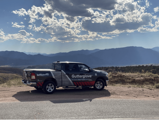 A Gutterglove-branded pickup truck, from a leading gutter guard manufacturer, is parked roadside with mountains and a partly cloudy sky in the background. The bright, scenic setting highlights natural beauty and open space.